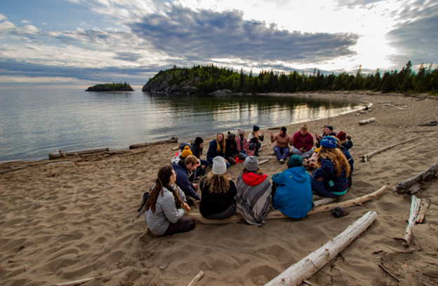 Participants de la cohorte Ocean Bridge Great Lakes 2019 assis en cercle sur une plage du lac Supérieur.